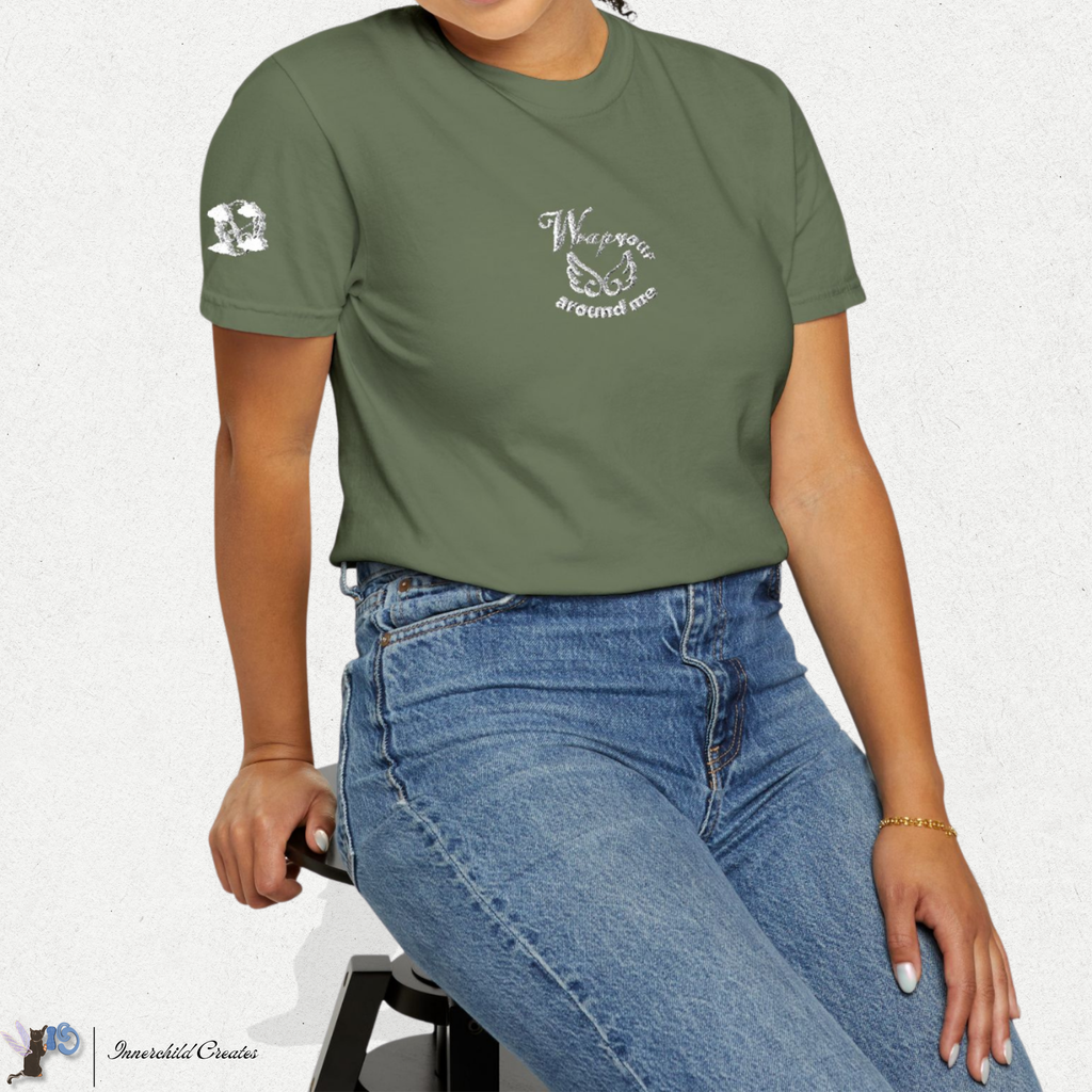 Person wearing a green t-shirt with text and graphics, sitting on a stool against a white background. White embroidery wings & clouds.